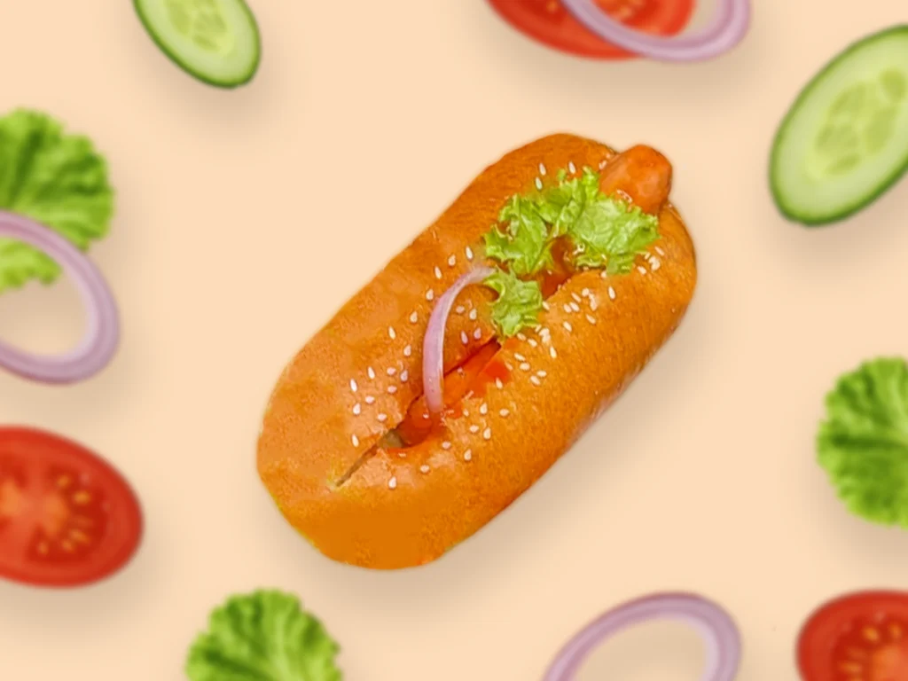 Soft sausage bun with fresh tomato, onion slices, and salad leaf on a plate